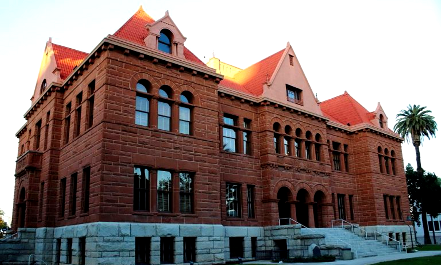 Picture of red bricked courthouse. There are palm trees in front. 